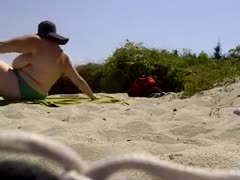 On a naked beach, a topless woman with enormous mambos is seen lounging.